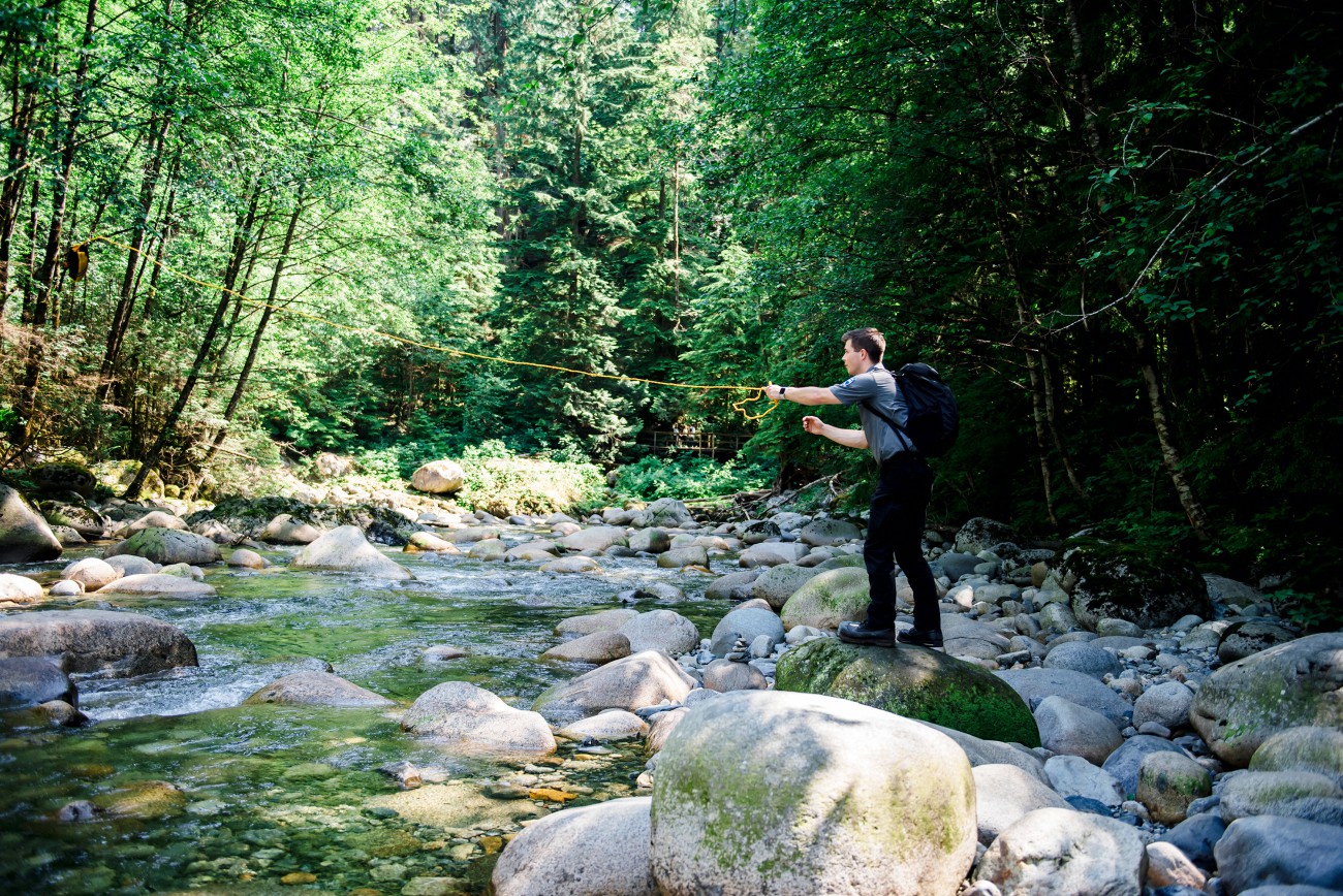 A young Ranger standing on a creek-side boulder demonstrates throwing a yellow life line that can be used to save victims in distress.