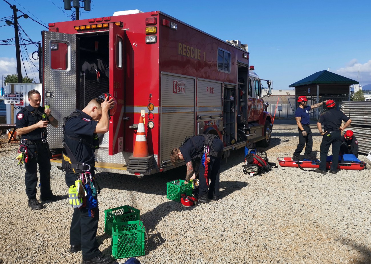 A group of  firefighters in blue uniforms and red helmets prepare their gear.