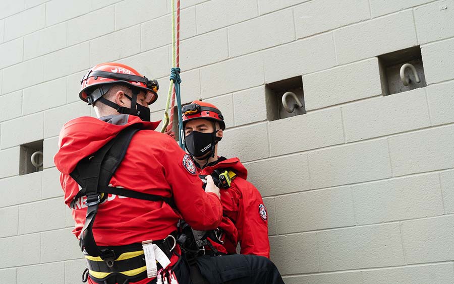 Two firefighters wearing mask practise harness rescue.