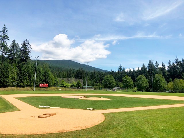 A pristine-looking baseball field surrounded by trees and a mountainous backdrop.