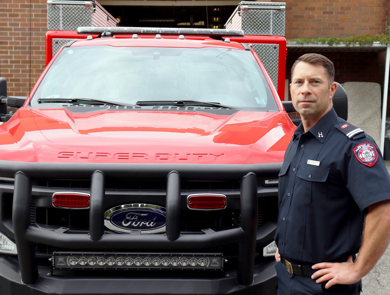 A firefighter in a blue uniform stands in front of a red pickup truck that is designed for off-road rescues and fire fighting.