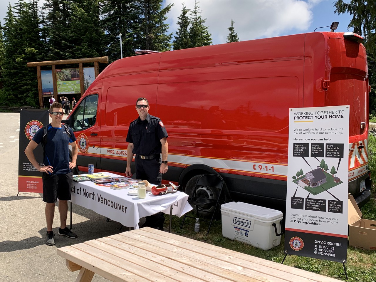 A pair of DNVFRS firefighters stand in front of a red Fire Investigation van as they share wildfire information with residents.