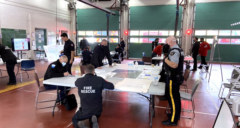 A group of DNVFRS personnel and RCMP around a table looking at a map.