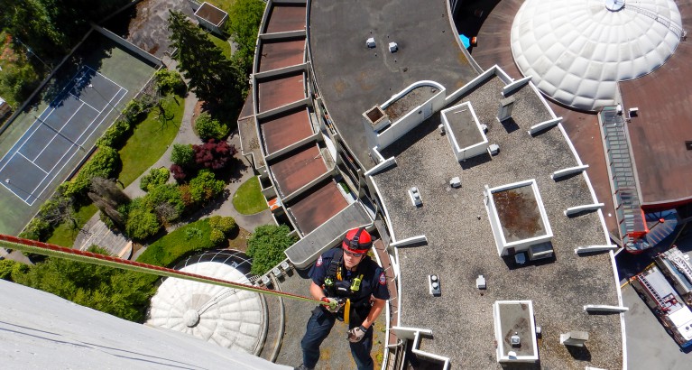 A district firefighter rappelling down a tall concrete building.
