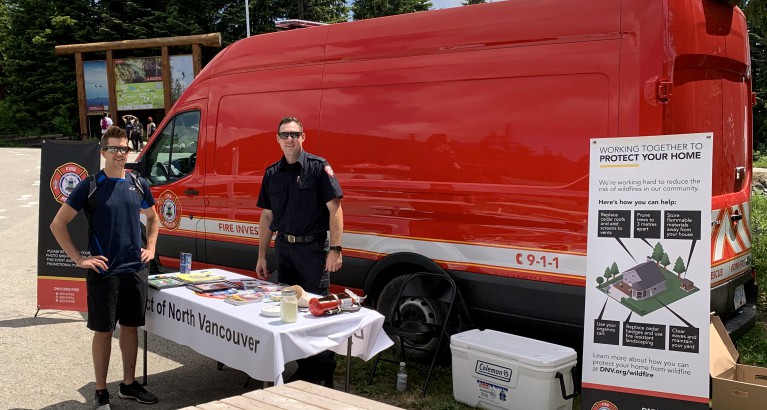 A pair of DNVFRS firefighters stand in front of a red Fire Investigation van as they share wildfire information with residents.