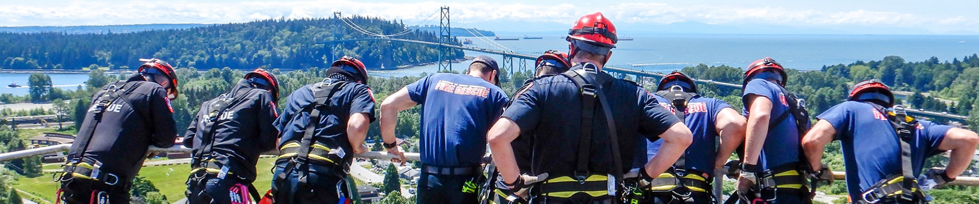 A group of firefighters clad in blue uniforms look over the edge of a tall building.