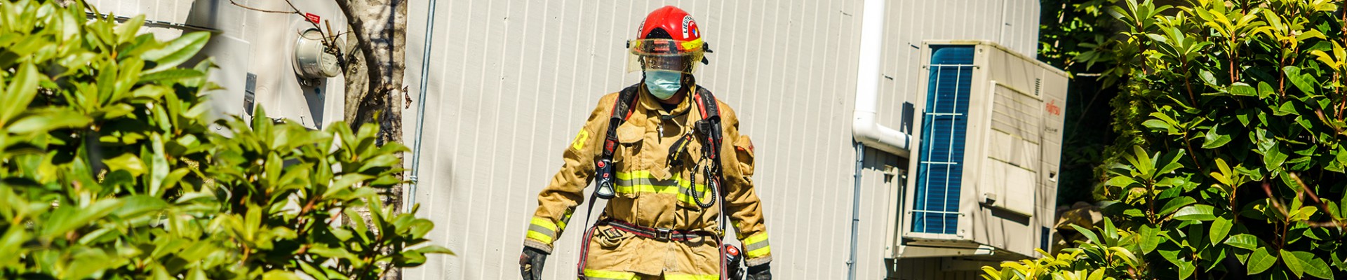 A firefighter in full gear stands outside a building.