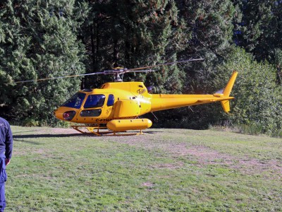 A yellow Talon helicopter in a field prepares for takeoff. 