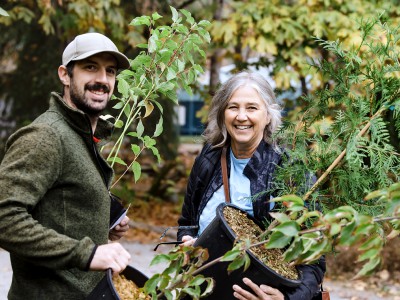 A smiling man and woman hold up potted trees they received as part of the Urban Tree Canopy Program. 