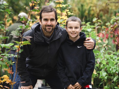 A  father and son with smiles on their faces pose in an outdoor nursery.