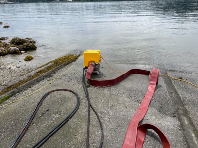 A red District of North Vancouver Fire Rescue Services pickup truck with a trailer that is loaded with a HydroSub-60 submersible pump used for access water from an open source such as the ocean or a river. 