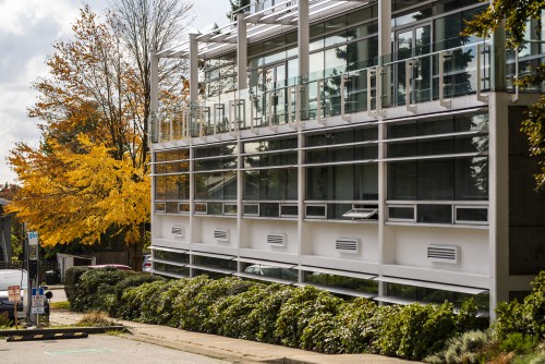 A modern glass and steel buildings with fall-hued trees in the foreground.