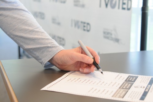A closeup of a a voter's hand casting an election ballot.