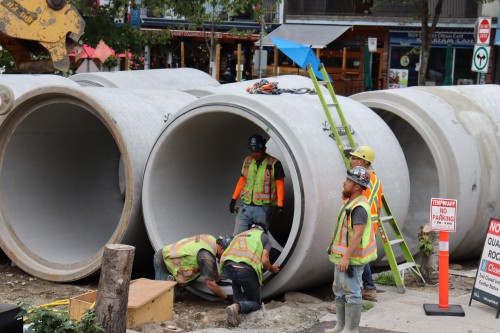 Construction workers unload giant cement culvert pipe pieces. 