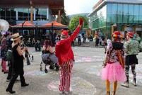A clown in striped pants wave to event goers in a plaza area.