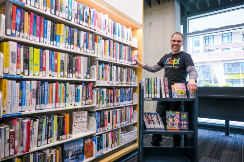 One staff wearing a black t-shirt with NVDPL logo taking out a book from a shelf