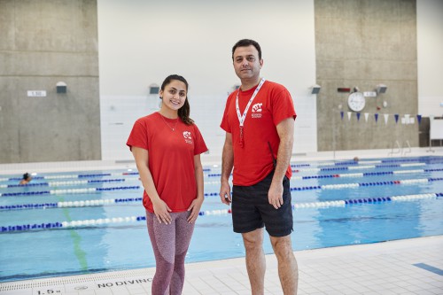 Two staff wearing red t-shirts with a NVRC logo standing in front of a swimming pool 
