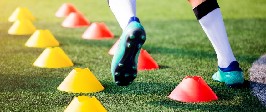 A closeup of a soccer player's feet on a turf field with red a yellow drill cones.